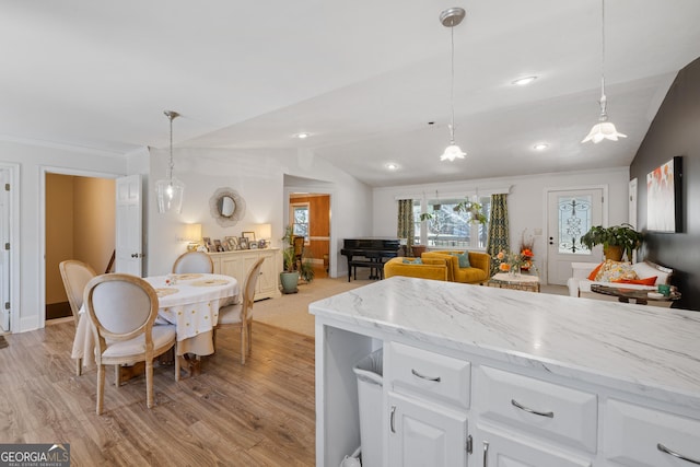 kitchen with pendant lighting, lofted ceiling, light stone counters, light wood-style floors, and white cabinets