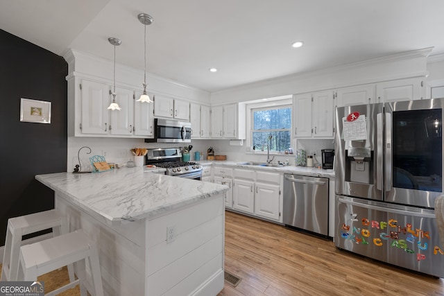 kitchen featuring a peninsula, a sink, stainless steel appliances, light wood-style floors, and white cabinetry