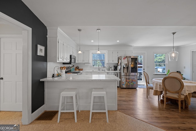 kitchen with appliances with stainless steel finishes, a peninsula, wood finished floors, hanging light fixtures, and white cabinets