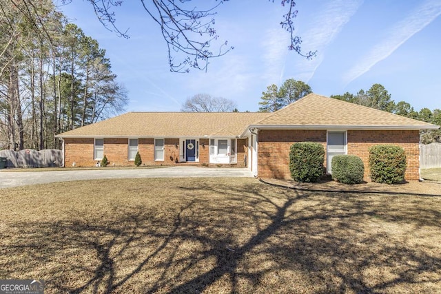 single story home with a shingled roof, brick siding, fence, and a front lawn