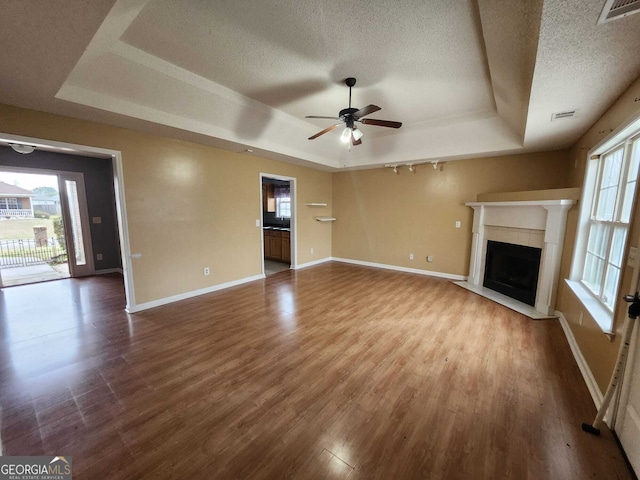 unfurnished living room featuring visible vents, a tray ceiling, dark wood finished floors, and a textured ceiling