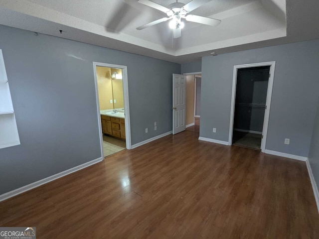 unfurnished bedroom featuring a tray ceiling, wood finished floors, and baseboards