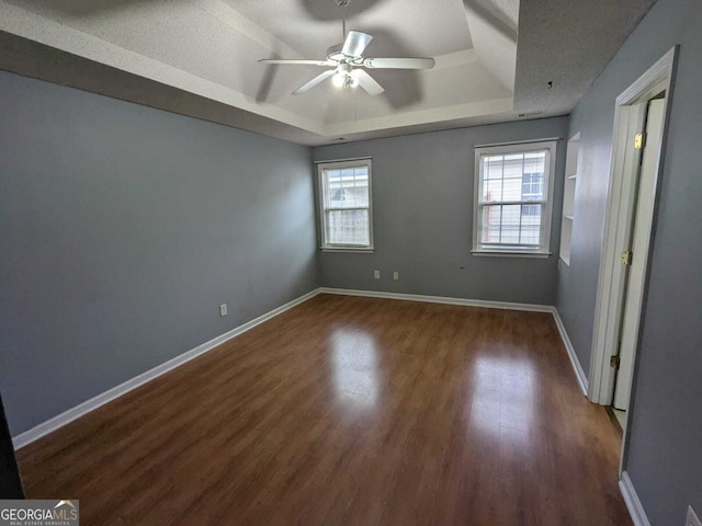 empty room featuring a tray ceiling, ceiling fan, a textured ceiling, wood finished floors, and baseboards