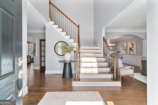 entrance foyer featuring crown molding, stairway, arched walkways, and wood finished floors