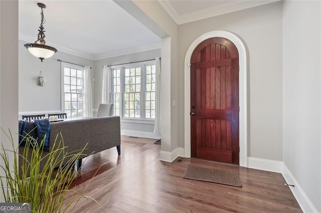 entrance foyer featuring baseboards, wood finished floors, arched walkways, and ornamental molding