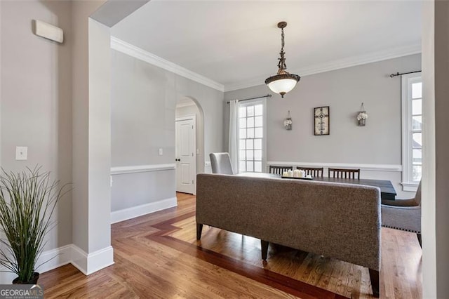 dining space featuring arched walkways, crown molding, baseboards, and wood finished floors