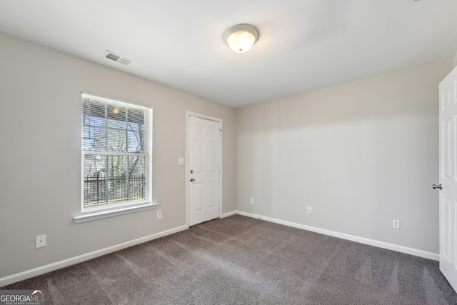 empty room featuring dark colored carpet, visible vents, and baseboards