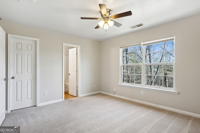 unfurnished bedroom with baseboards, visible vents, connected bathroom, light colored carpet, and ceiling fan