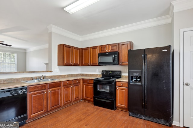 kitchen with crown molding, brown cabinetry, a sink, wood finished floors, and black appliances