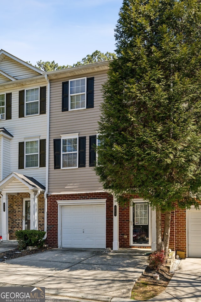 townhome / multi-family property featuring a garage, concrete driveway, and brick siding