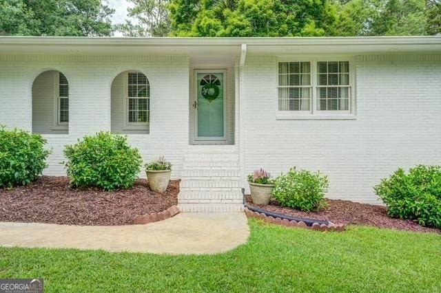 view of exterior entry with brick siding and a yard