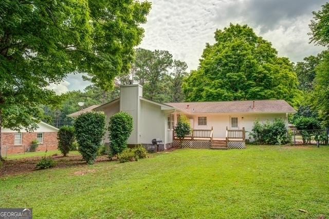 back of house with a chimney, a deck, and a yard