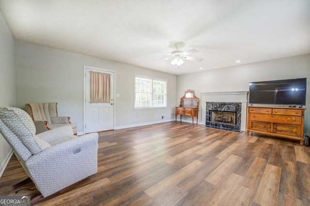 living area featuring a high end fireplace, wood finished floors, a ceiling fan, and baseboards