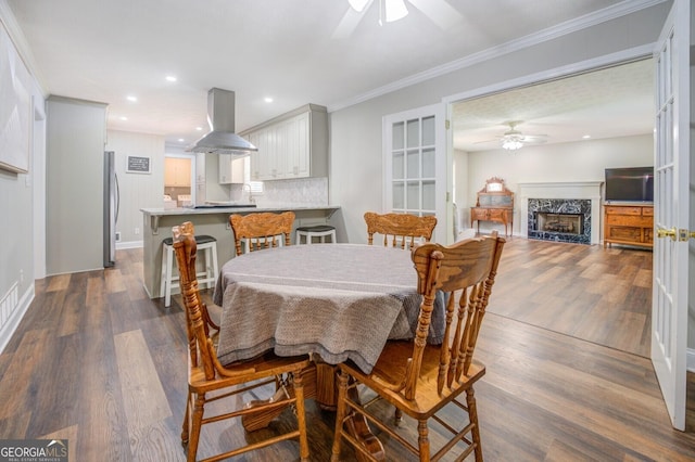 dining area with a premium fireplace, ornamental molding, dark wood finished floors, and a ceiling fan