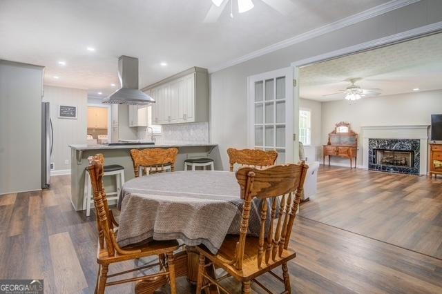 dining area featuring ceiling fan, a fireplace, dark wood finished floors, and crown molding