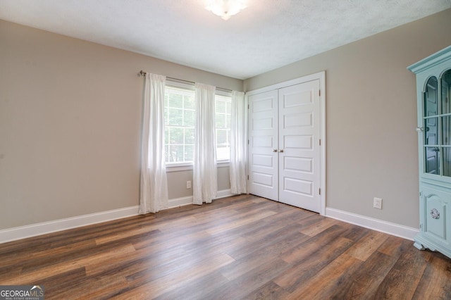 unfurnished bedroom with a closet, dark wood-style flooring, and baseboards