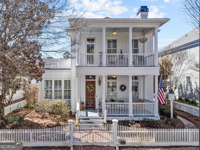 greek revival house with a porch, a fenced front yard, a chimney, and a balcony