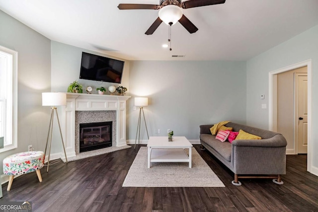 living area featuring dark wood-style floors, a glass covered fireplace, visible vents, and baseboards