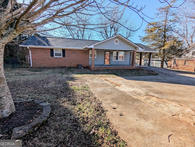 ranch-style house with covered porch, roof with shingles, concrete driveway, and brick siding