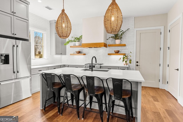 kitchen featuring light wood-style flooring, visible vents, stainless steel refrigerator with ice dispenser, custom exhaust hood, and open shelves