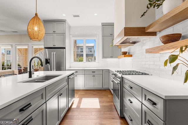 kitchen featuring open shelves, gray cabinets, custom range hood, appliances with stainless steel finishes, and a sink