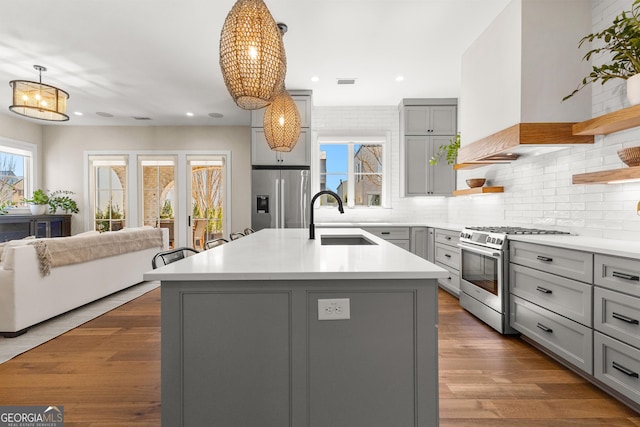 kitchen with appliances with stainless steel finishes, gray cabinetry, premium range hood, open shelves, and a sink