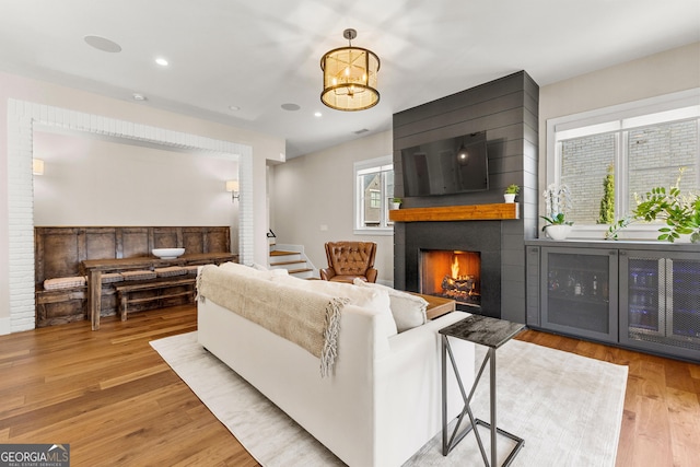 living area featuring light wood-style flooring, a notable chandelier, a large fireplace, recessed lighting, and stairs