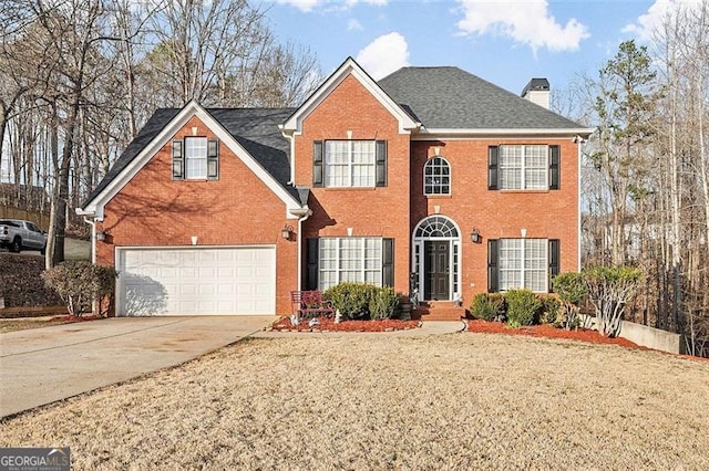 colonial home featuring an attached garage, a chimney, concrete driveway, and brick siding