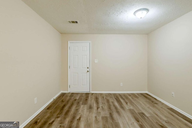 empty room with visible vents, a textured ceiling, baseboards, and wood finished floors