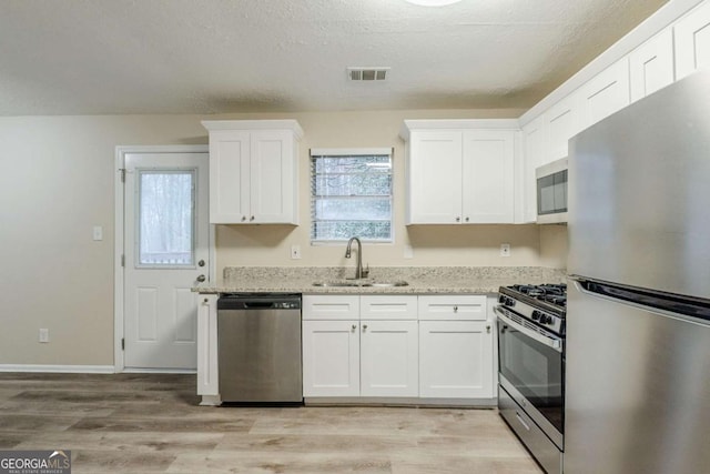 kitchen featuring visible vents, light wood-style flooring, stainless steel appliances, white cabinetry, and a sink