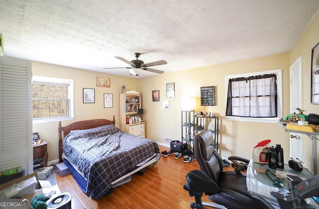 bedroom featuring a textured ceiling, multiple windows, wood finished floors, and baseboards