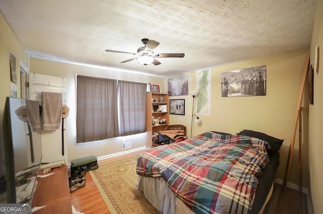 bedroom featuring ceiling fan, a textured ceiling, baseboards, and wood finished floors