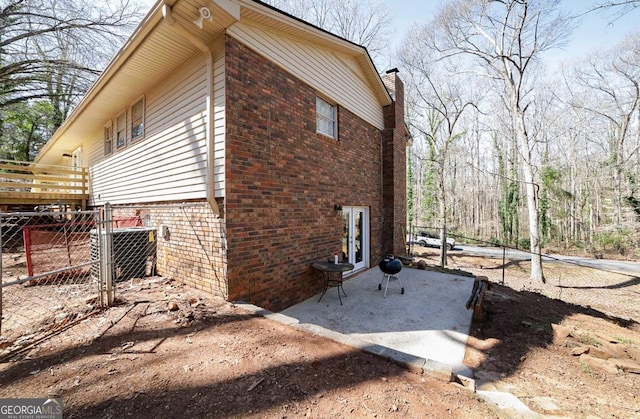 view of side of home featuring brick siding, fence, a chimney, and central AC unit