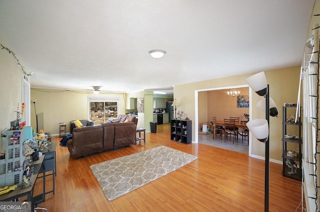 living room with ceiling fan with notable chandelier, baseboards, and wood finished floors