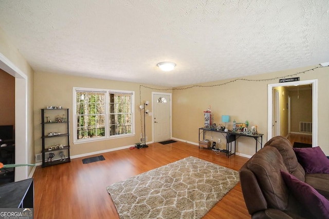 living room with visible vents, a textured ceiling, baseboards, and wood finished floors