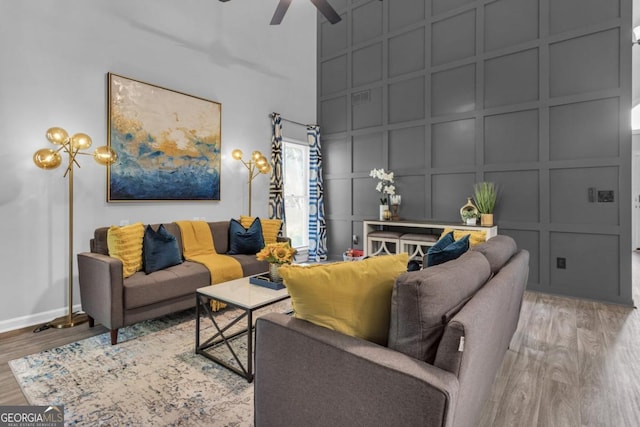 living room with baseboards, a ceiling fan, wood finished floors, a high ceiling, and a decorative wall