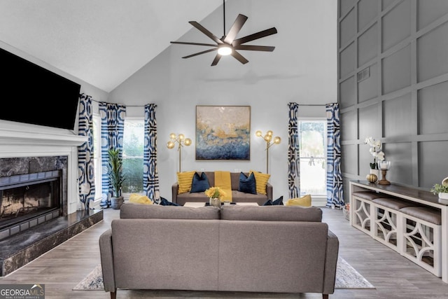 living room with ceiling fan, a premium fireplace, wood finished floors, and a decorative wall