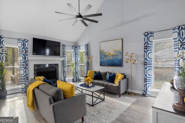 living area with ceiling fan, high vaulted ceiling, a high end fireplace, baseboards, and light wood-type flooring