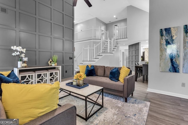 living area featuring a decorative wall, a high ceiling, wood finished floors, baseboards, and stairs