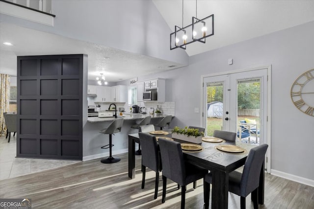 dining space featuring light wood-type flooring, high vaulted ceiling, baseboards, and french doors