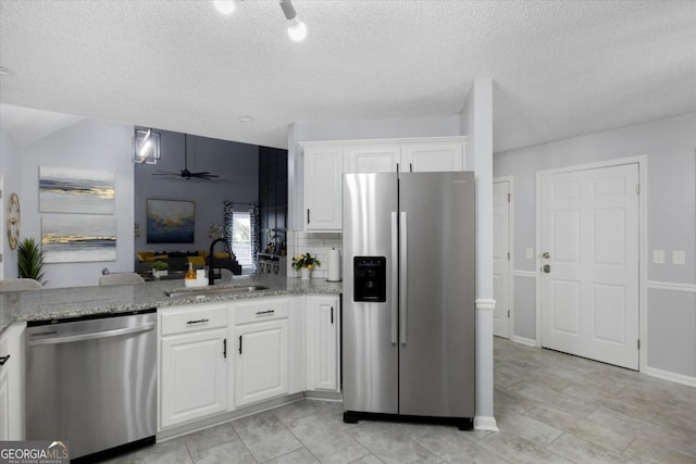 kitchen with ceiling fan, light stone counters, stainless steel appliances, a sink, and white cabinetry