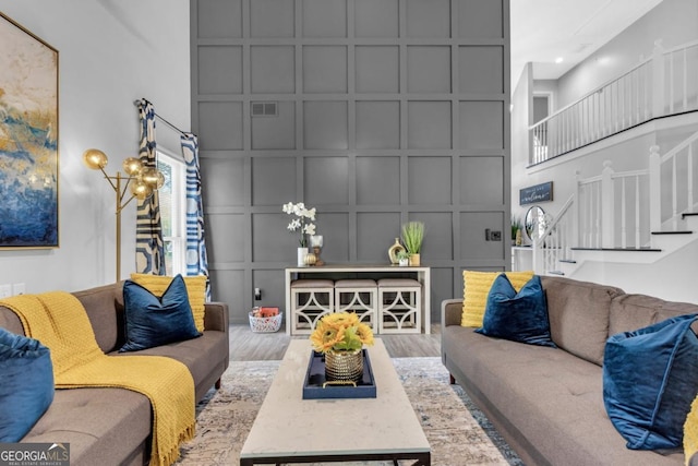 living area featuring visible vents, a decorative wall, stairway, a high ceiling, and wood finished floors