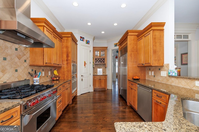 kitchen featuring high end appliances, brown cabinetry, ornamental molding, light stone countertops, and wall chimney range hood