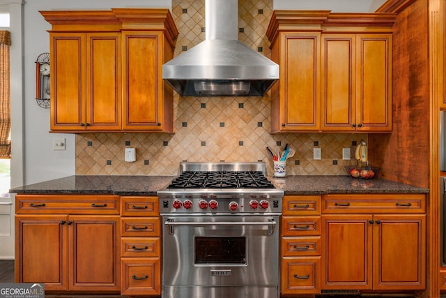 kitchen featuring designer stove, brown cabinets, backsplash, and wall chimney exhaust hood