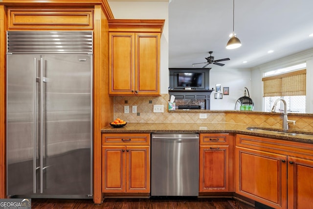 kitchen featuring tasteful backsplash, brown cabinetry, appliances with stainless steel finishes, dark stone countertops, and a sink