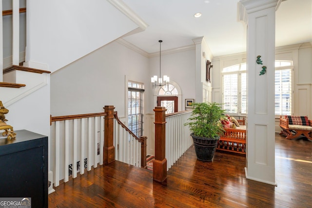 staircase with a decorative wall, wood finished floors, ornamental molding, an inviting chandelier, and ornate columns