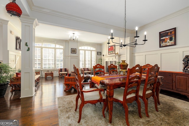 dining room featuring a decorative wall, dark wood-style flooring, a fireplace, decorative columns, and crown molding