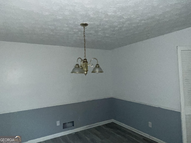 unfurnished dining area featuring a textured ceiling, dark wood-style flooring, baseboards, vaulted ceiling, and an inviting chandelier