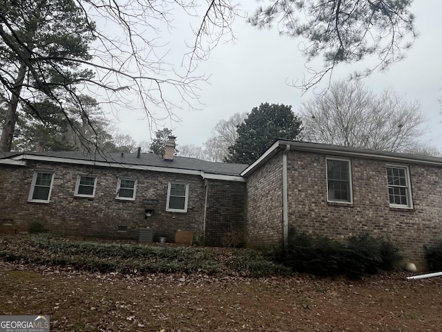 back of house with crawl space, brick siding, and a chimney