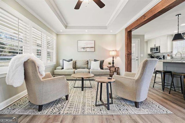 living room featuring baseboards, a tray ceiling, light wood-style flooring, ceiling fan, and crown molding